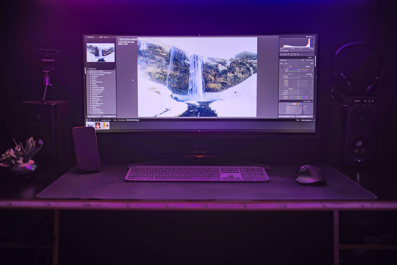 Stylish computer setup with a large monitor showcasing photo editing software in a dimly lit room.